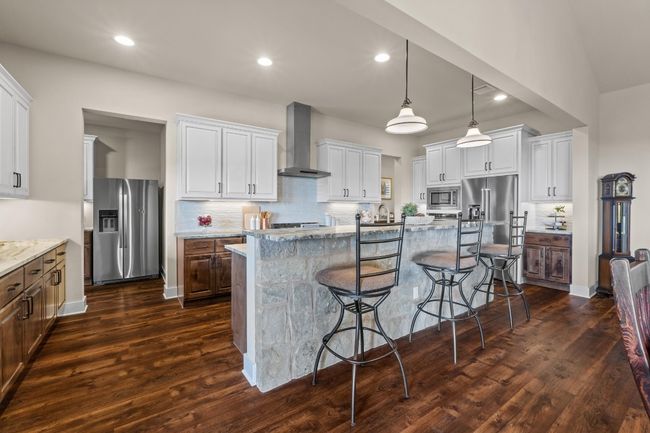 Kitchen with wall chimney exhaust hood, dark wood finished floors, backsplash, appliances with stainless steel finishes, and a breakfast bar area | Image 10