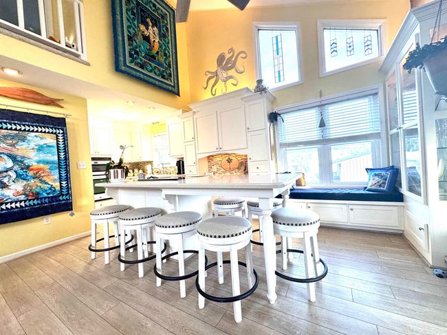 Kitchen featuring a towering ceiling, light wood-style flooring, a breakfast bar, light countertops, and white cabinetry | Image 18