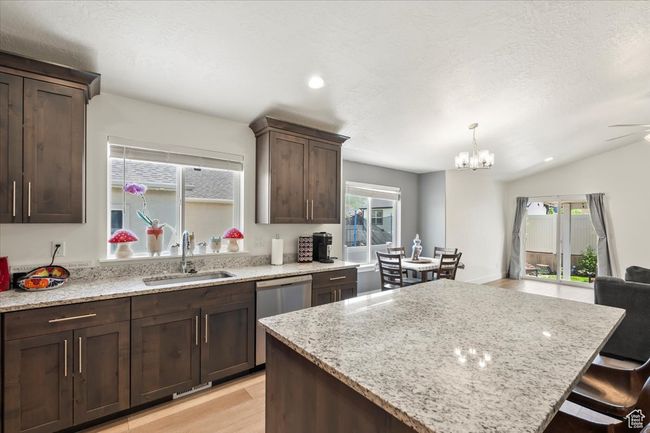 Kitchen featuring a sink, stainless steel dishwasher, a kitchen island, dark brown cabinets, and light stone countertops | Image 9