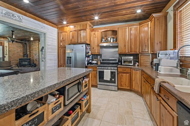 Kitchen featuring appliances with stainless steel finishes, wooden ceiling, a wood stove, under cabinet range hood, and a sink | Image 10
