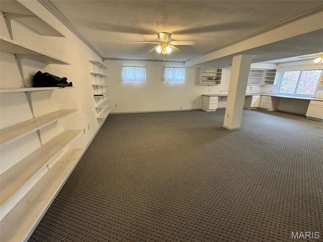 Basement featuring ornamental molding, dark colored carpet, ceiling fan, and built in desk | Image 39