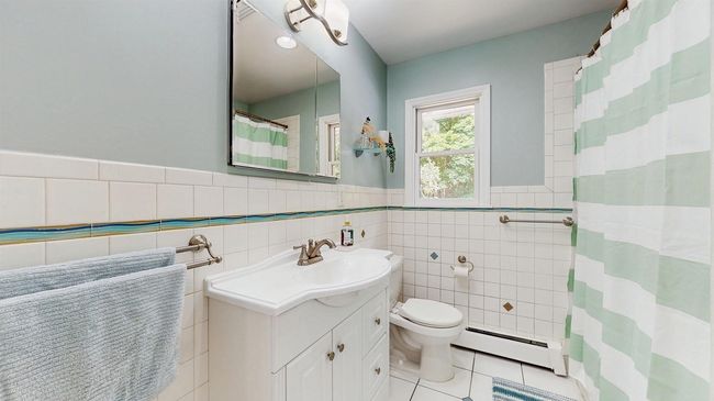 1st Floor Bathroom with a baseboard heating unit, vanity, toilet, bathtub and ceramic tiled walls, with ceramic tile patterned floors. | Image 20