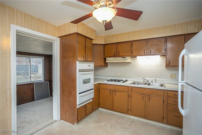 Kitchen with white appliances, a warming drawer, under cabinet range hood, light countertops, and ceiling fan | Image 17