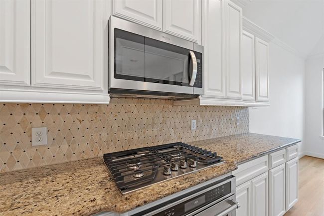 This close-up showcases the stylish gas stovetop with a built-in microwave above, complemented by a custom backsplash that adds a touch of elegance to the kitchen. | Image 4