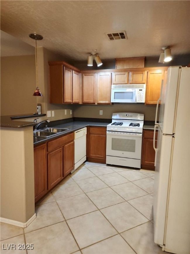 Kitchen with a sink, light tile patterned floors, visible vents, white appliances, and dark countertops | Image 8