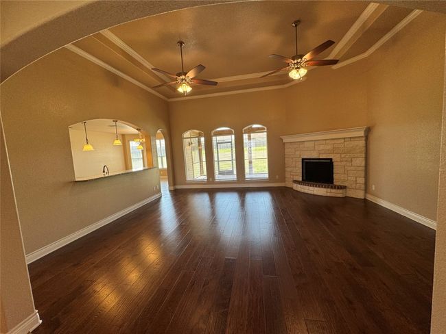 Unfurnished living room with crown molding, baseboards, a raised ceiling, a ceiling fan, and dark wood-style flooring | Image 5