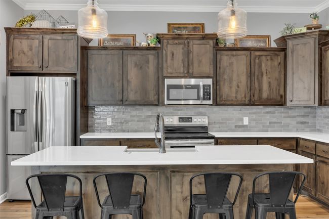 Kitchen featuring tasteful backsplash, a breakfast bar area, ornamental molding, light wood-style floors, and stainless steel appliances | Image 16