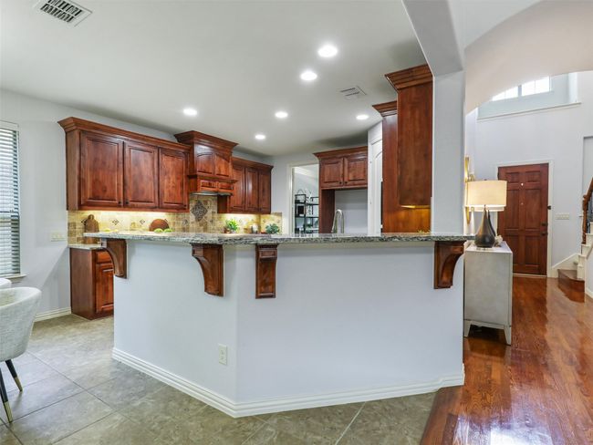 Kitchen featuring a breakfast bar area, backsplash, light stone countertops, recessed lighting, and a peninsula | Image 12