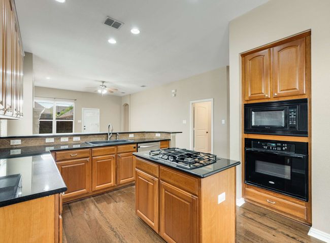 Kitchen with black appliances, wood finished floors, a peninsula, a ceiling fan, and recessed lighting | Image 12