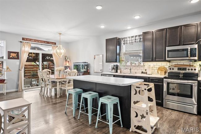Kitchen with appliances with stainless steel finishes, a kitchen island, light countertops, a breakfast bar, and backsplash | Image 13