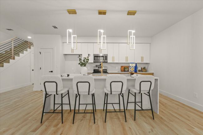 Kitchen with appliances with stainless steel finishes, white cabinets, a large island, and light wood finished floors | Image 5