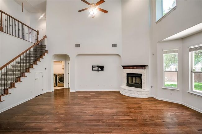 Unfurnished living room featuring washer / clothes dryer, a ceiling fan, a high ceiling, wood finished floors, and a fireplace | Image 10