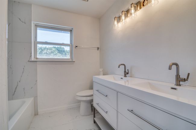 Full bath with marble finish flooring, double vanity, toilet, a bath, and baseboards | Image 23