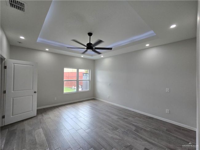 Empty room with a tray ceiling, ceiling fan, dark wood-style floors, recessed lighting, and baseboards | Image 13