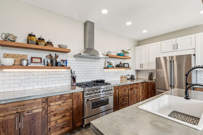Kitchen with wall chimney range hood, appliances with stainless steel finishes, open shelves, white cabinets, and decorative backsplash | Image 20