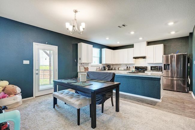 Kitchen featuring stainless steel refrigerator with ice dispenser, a chandelier, white cabinets, a textured wall, and black range with electric cooktop | Image 15