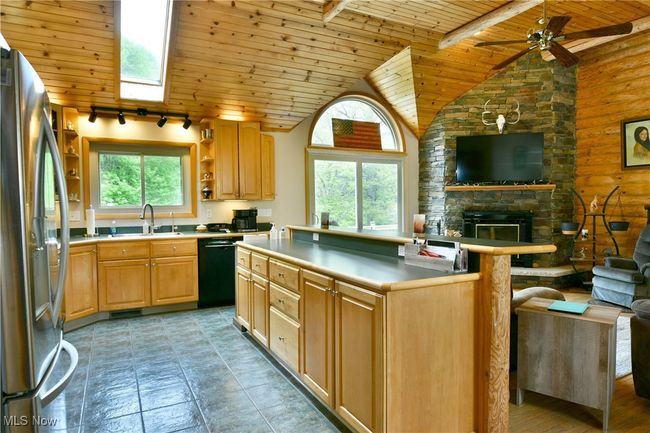 Kitchen with wooden ceiling, freestanding refrigerator, black dishwasher, vaulted ceiling, and a sink | Image 12