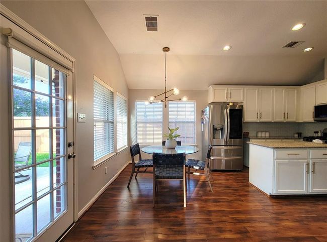 Bright and welcoming kitchen with modern appliances, white cabinetry, and warm wood floors. The dining area features a stylish light fixture and a clear view of the fenced backyard through large windows and a glass door. Ideal for family gatherings and entertaining. | Image 10