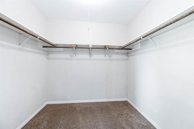 This is a spacious walk-in closet with white walls, carpeted flooring, and multiple hanging rods for ample storage. | Image 22