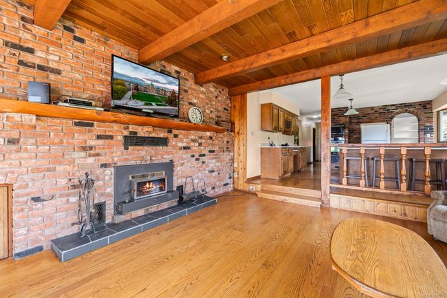 Unfurnished living room with wood finished floors, wood ceiling with exposed beams, brick wall, a wood stove, and a fireplace | Image 16