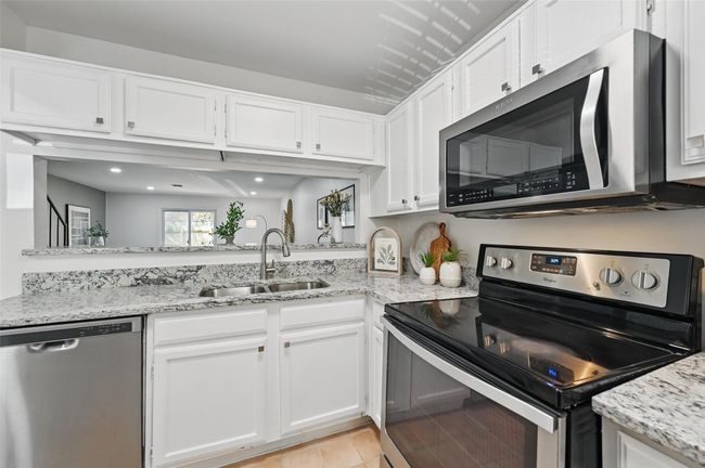 Kitchen featuring appliances with stainless steel finishes, a sink, white cabinetry, and light stone counters | Image 4