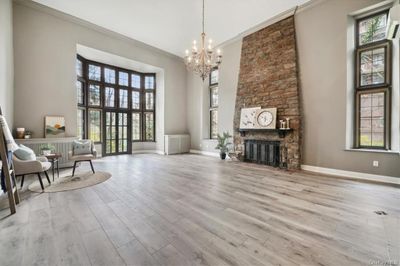 Living area with a towering ceiling, a stone fireplace, crown molding, light wood-type flooring, and an inviting chandelier | Image 2