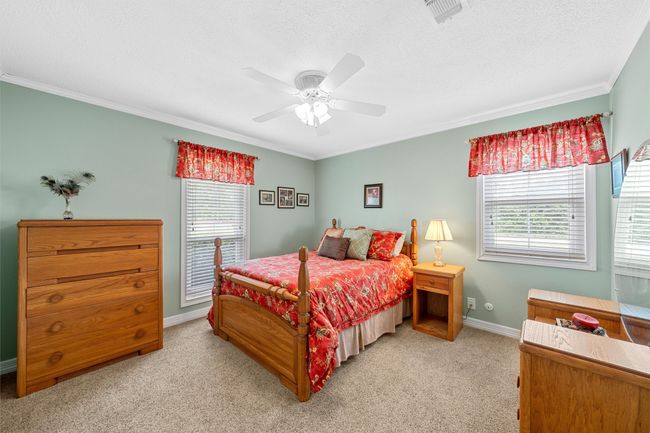 Bedroom featuring multiple windows, crown molding, light colored carpet, a textured ceiling, and ceiling fan | Image 24