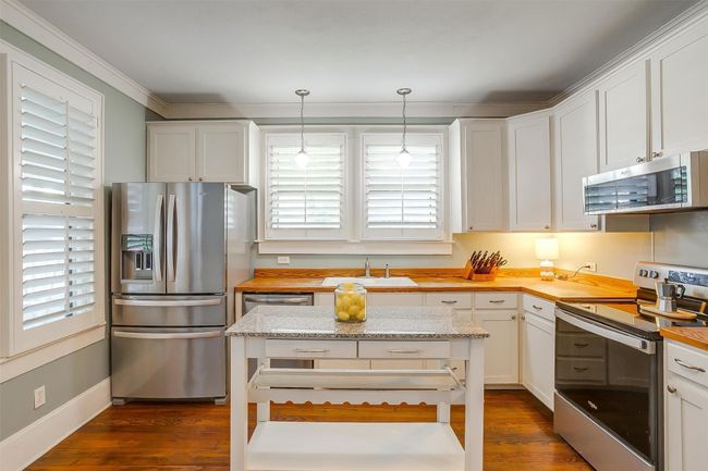 Kitchen with stainless steel appliances, butcher block countertops, dark wood-style flooring, white cabinetry, and crown molding | Image 29