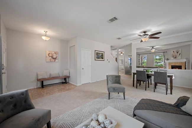 Living room with light carpet, a ceiling fan, baseboards, and a lit fireplace | Image 5