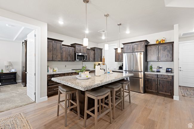 Kitchen featuring stainless steel appliances, dark brown cabinetry, light wood-style floors, a kitchen breakfast bar, and a kitchen island with sink | Image 47