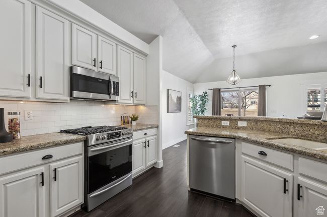 Kitchen featuring light stone counters, pendant lighting, stainless steel appliances, lofted ceiling, and white cabinets | Image 13