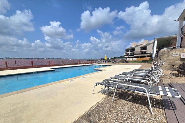 This photo showcases a waterfront property with a spacious outdoor pool, surrounded by lounge chairs. The setting offers stunning lake views, a relaxing ambiance, and nearby residential buildings, ideal for a serene lifestyle. | Image 29