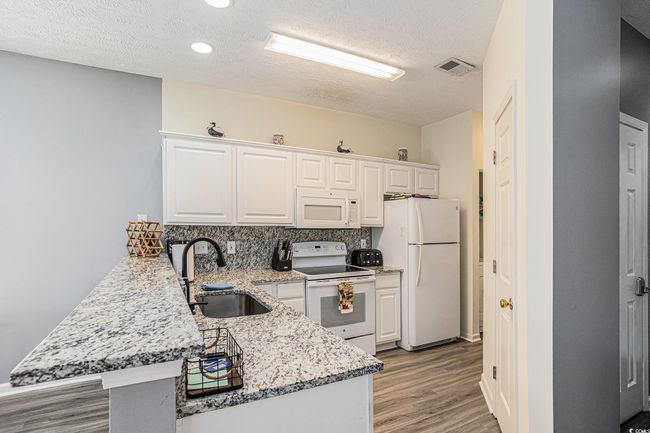 Kitchen with white appliances, a peninsula, light wood-style floors, white cabinetry, and a textured ceiling | Image 10