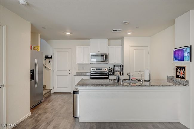 Kitchen featuring appliances with stainless steel finishes, a peninsula, light stone countertops, white cabinetry, and light wood-style flooring | Image 10