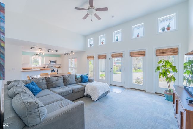 living area with a towering ceiling, rail lighting, a ceiling fan, and light carpet | Image 6