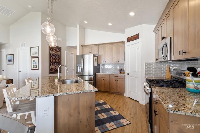 Kitchen featuring appliances with stainless steel finishes, a kitchen breakfast bar, light wood-style flooring, high vaulted ceiling, and tasteful backsplash | Image 7
