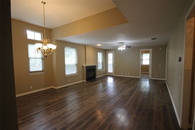 Unfurnished living room with dark wood-style floors, a fireplace with flush hearth, a chandelier, and ceiling fan | Image 5