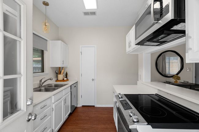 Kitchen featuring stainless steel appliances, light countertops, white cabinetry, and dark wood finished floors | Image 12