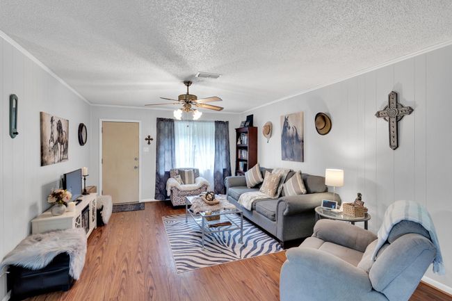 Living area featuring ornamental molding, a textured ceiling, wood finished floors, and a ceiling fan | Image 7