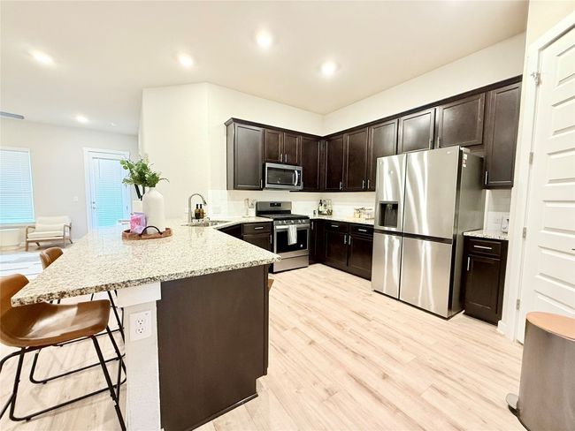Kitchen with a sink, a peninsula, stainless steel appliances, dark brown cabinetry, and light stone countertops | Image 8