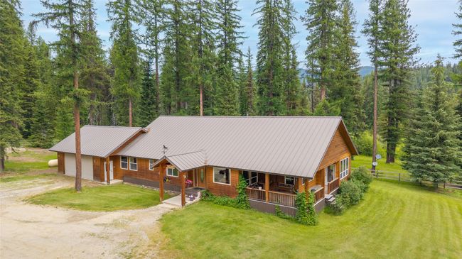 View of front of house featuring dirt driveway, a forest view, an attached garage, and a metal roof | Image 19