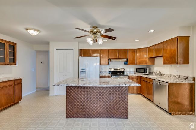 Kitchen featuring a ceiling fan, a sink, brown cabinets, stainless steel appliances, and under cabinet range hood | Image 5
