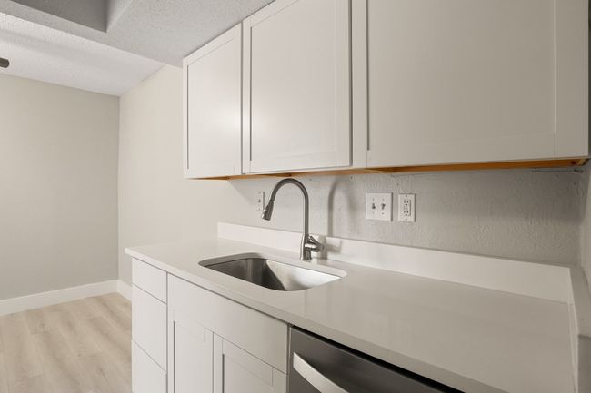 Kitchen with light wood-type flooring, light countertops, white cabinetry, a textured ceiling, and stainless steel dishwasher | Image 7