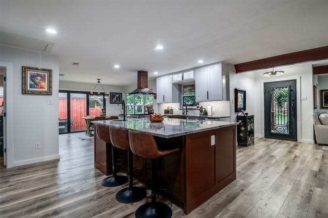 Kitchen with wall chimney exhaust hood, stone countertops, light wood-style flooring, a spacious island, and a kitchen bar | Image 13