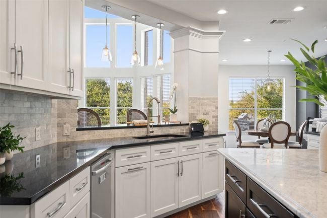 Kitchen featuring dark stone counters, a sink, stainless steel dishwasher, and visible vents | Image 6