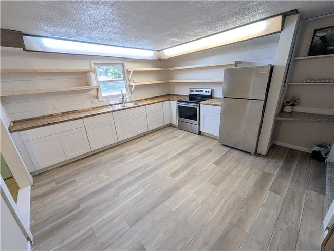 Kitchen featuring appliances with stainless steel finishes, open shelves, a sink, a textured ceiling, and wooden counters | Image 22