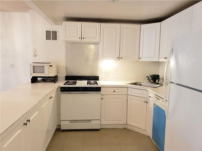 Kitchen with white appliances, white cabinetry, light tile patterned floors, and sink | Image 5