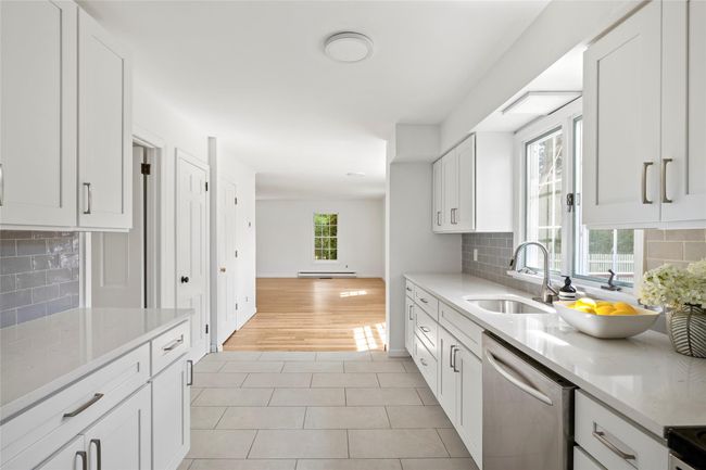 Kitchen with a sink, tasteful backsplash, light tile patterned floors, white cabinets, and stainless steel dishwasher | Image 9