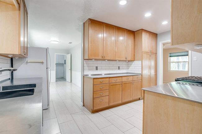 Kitchen featuring light brown cabinets, dual sinks, decorative backsplash, stainless steel counters, and recessed lighting | Image 14