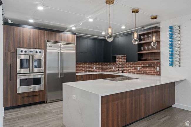 Kitchen featuring appliances with stainless steel finishes, pendant lighting, sink, LVP flooring, and kitchen peninsula with induction cooktop | Image 8